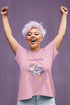 Ein galoppierendes Einhorn mit bunter Mähne ist auf einem T-Shirt mit vielen bunten Sternen zu sehen. Die Dame hat lila Haare.