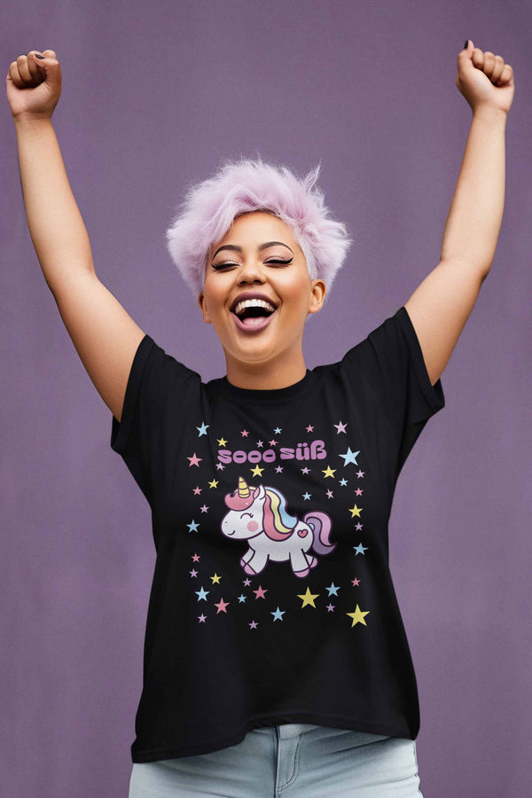 Auf einem T-Shirt galoppiert ein Einhorn durch die Sterne. Das T-Shirt hat die Farbe Schwarz. Vor lauter Freude reisst die Dame mit den lila Haaren die Hände in die Luft.